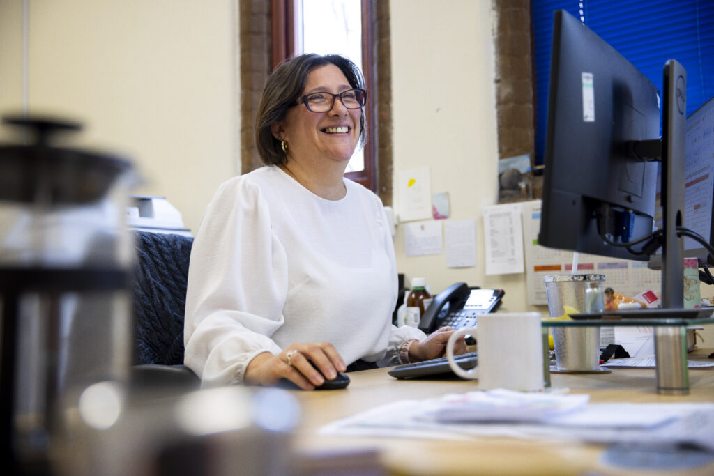 Office manager in a white top at her desk. She is smiling.